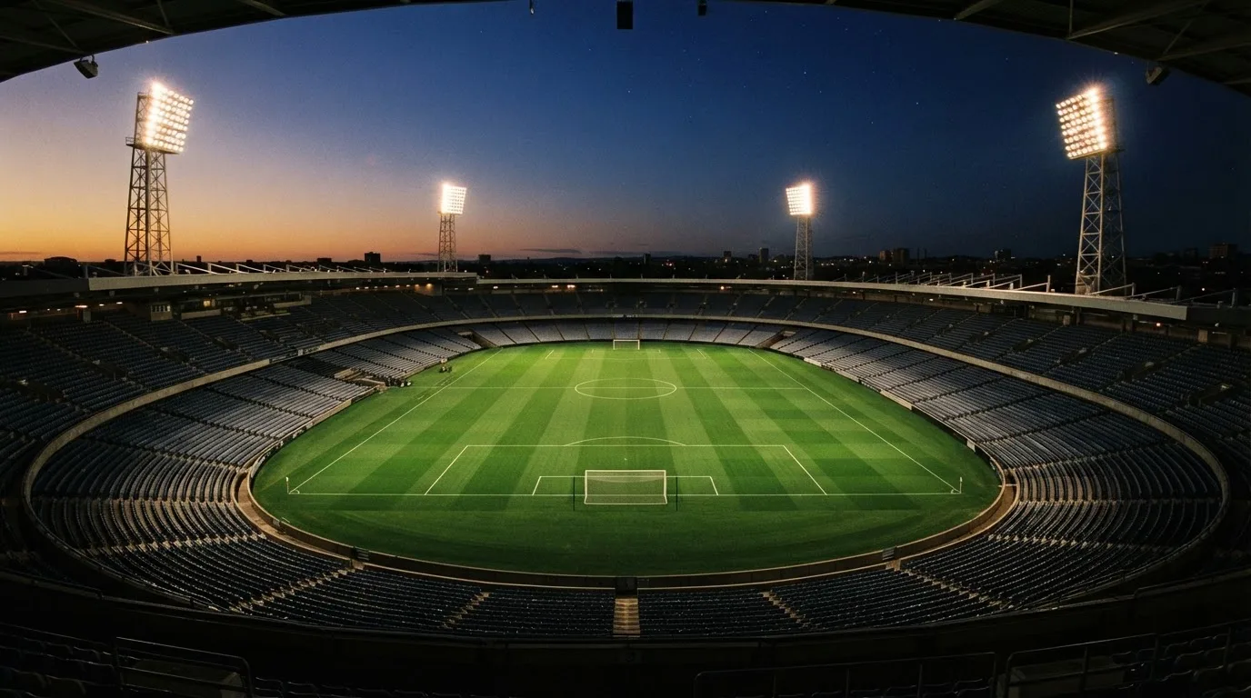 An empty football stadium with floodlight masts at dusk