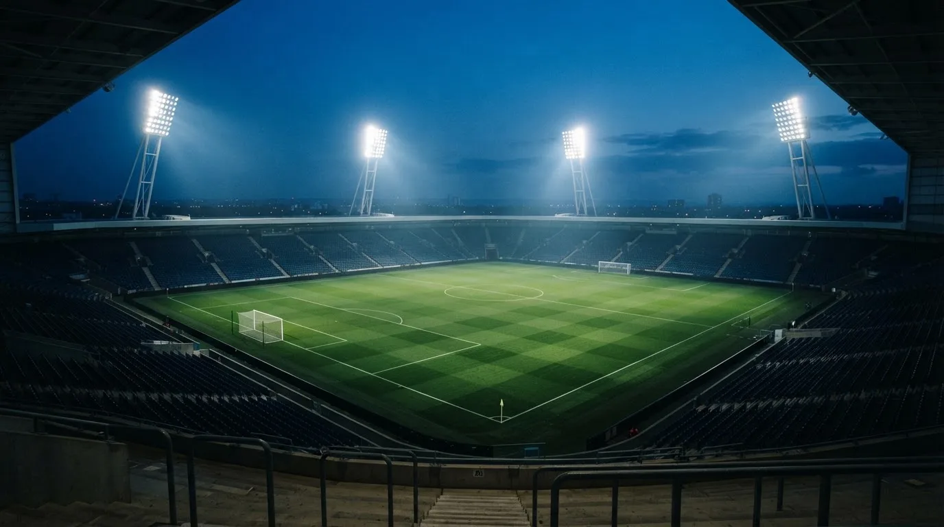 An empty football stadium with floodlight masts at dusk
