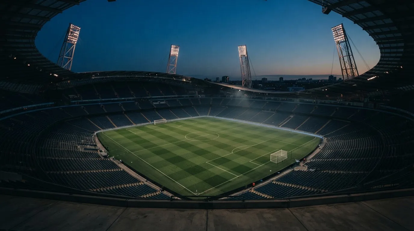 An empty football stadium with floodlight masts at dusk
