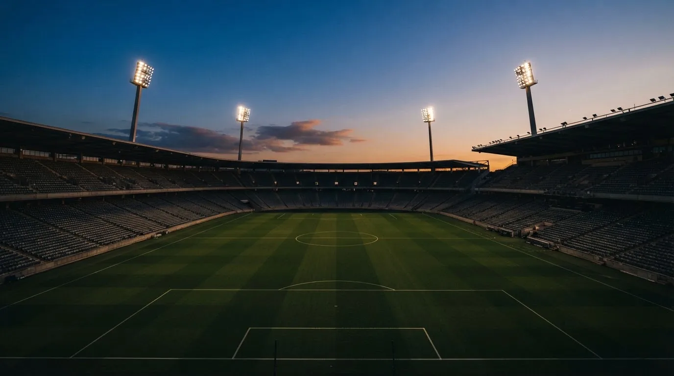 An empty football stadium with floodlight masts at dusk