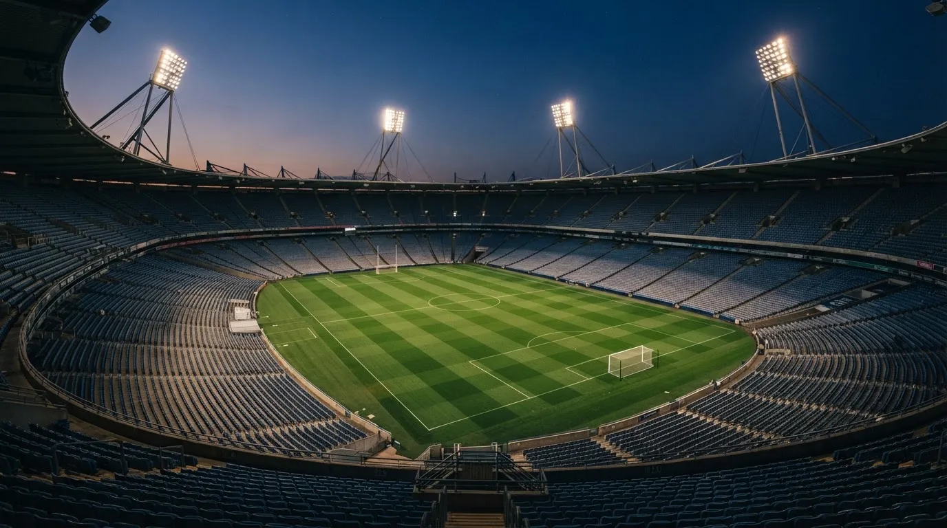 An empty football stadium with floodlight masts at dusk